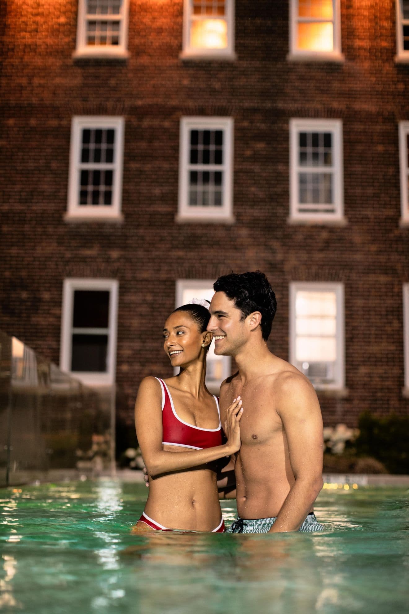 A man and a woman smiling in an outdoor hot tub with the spa building in the background