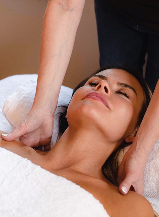 A close-up of a woman lying on a massage table while receiving a neck massage